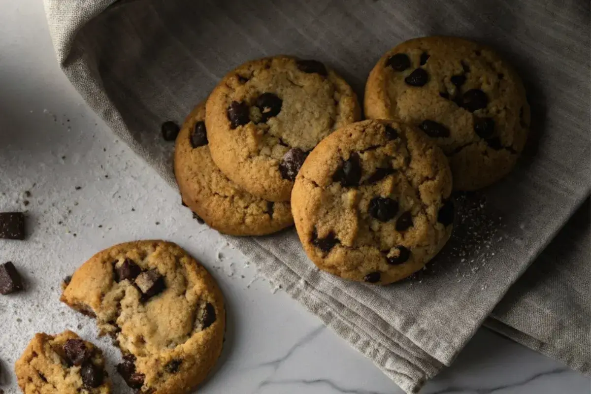 Gros plan sur des cookies sans œuf dorés et moelleux avec des pépites de chocolat fondantes, posés sur une table en bois foncé avec un verre de lait végétal à côté.