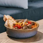 ne délicieuse portion d'axoa de veau dans un bol en céramique rustique, avec du veau tendre, des légumes colorés et une pincée de piment d'Espelette, accompagnée de riz chaud.