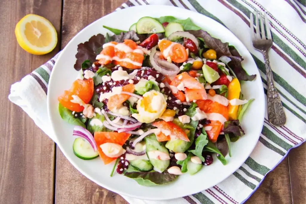 Elegant salad featuring thin slices of smoked salmon arranged over a bed of mixed greens, garnished with avocado, radish slices, and a drizzle of lemon vinaigrette, served in a white bowl with a fork on the side.