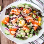 Elegant salad featuring thin slices of smoked salmon arranged over a bed of mixed greens, garnished with avocado, radish slices, and a drizzle of lemon vinaigrette, served in a white bowl with a fork on the side.