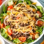 Salade Big Mac servie sur une assiette blanche avec viande hachée, cheddar fondu, salade iceberg, tomates, cornichons et sauce crémeuse.
