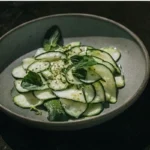 Salade de Concombre Fraîche et Gourmande servie sur une table rustique avec un verre d'eau citronnée.