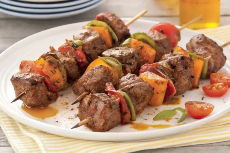 morceaux de bœuf marinés en train d’être enfilés sur des brochettes, avec des légumes frais