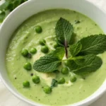 velouté de petits pois dans un bol blanc, garni de crème et de feuilles de menthe.